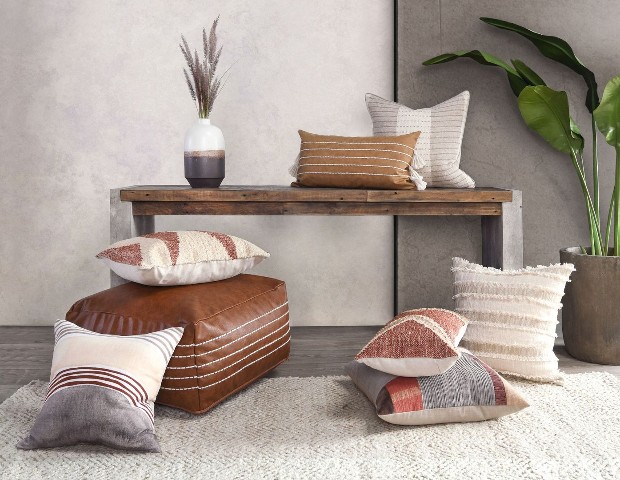 Numerous pillow varying in creams, pinks and greys on a off white rug and wooden bench