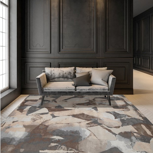A taupe and grey couch in front of a dark panel wall, with a multicolored earth toned rug