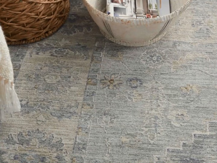 A grey and blue rug with a distressed floral pattern