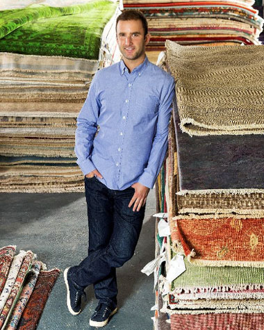 portrait of Noah Krinick leaning against stack of rugs