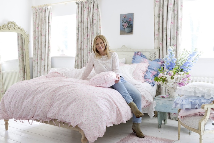 Photo of designer Rachel Ashwell sitting in a bedroom styled with Simply Shabby Chic home textiles for Target