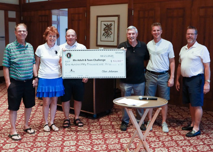 6 people (5 men and 1 woman) pose with a large check