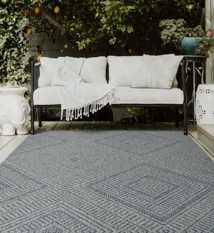 A patio set up with a black and white couch on a grey blue geometric patterned rug