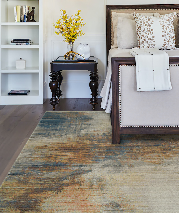 Image of a bed and nightstand on a grey, taupe and blue rug