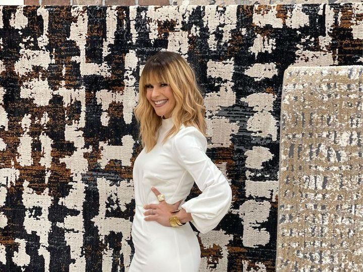 Stacy Garcia in a white dress, posing in front of earth tone colored rugs.