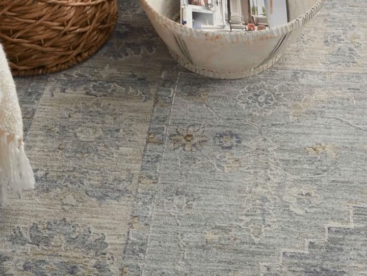 A grey and blue rug with a distressed floral pattern