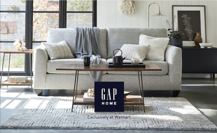 The GAP logo in front of a small coffee table and white couch with multiple pillows and a grey throw blanket